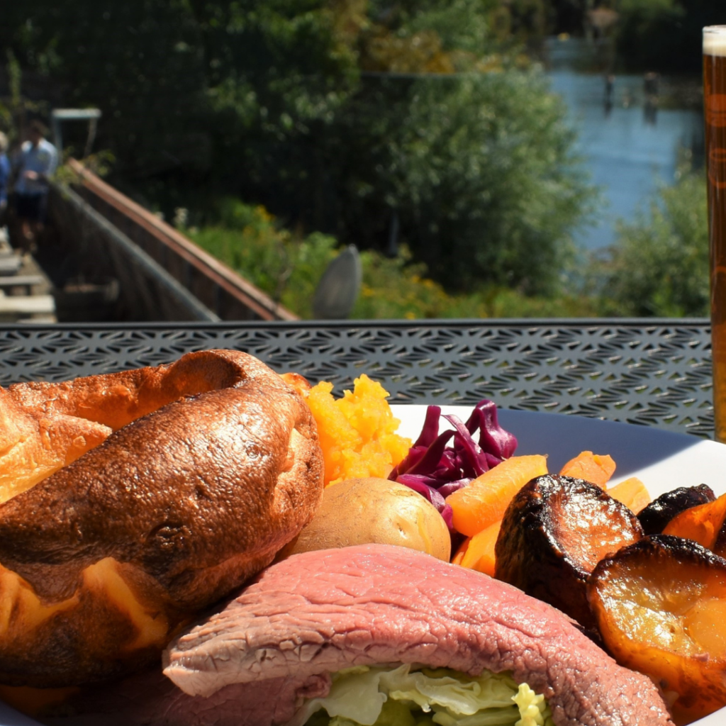 A roast carvery dinner served outside on a sunny day with a pint of beer and the river in the background