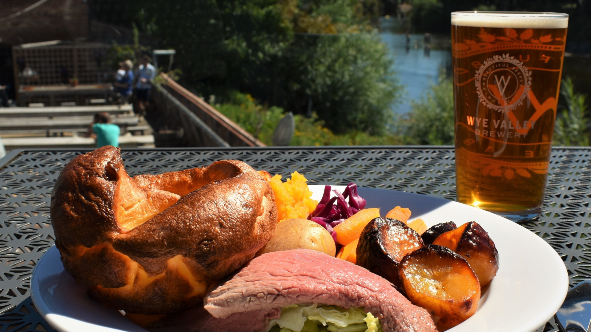 A roast carvery dinner served outside on a sunny day with a pint of beer and the river in the background