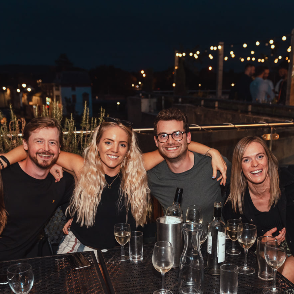 Two couples with drinks on a riverside terrace at night time